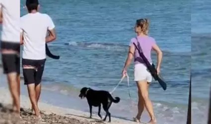 La mujer extranjera caminando por la playa con un rifle