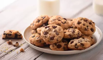 Pila de deliciosas galletas de chocolate en una placa blanca con botellas de lec